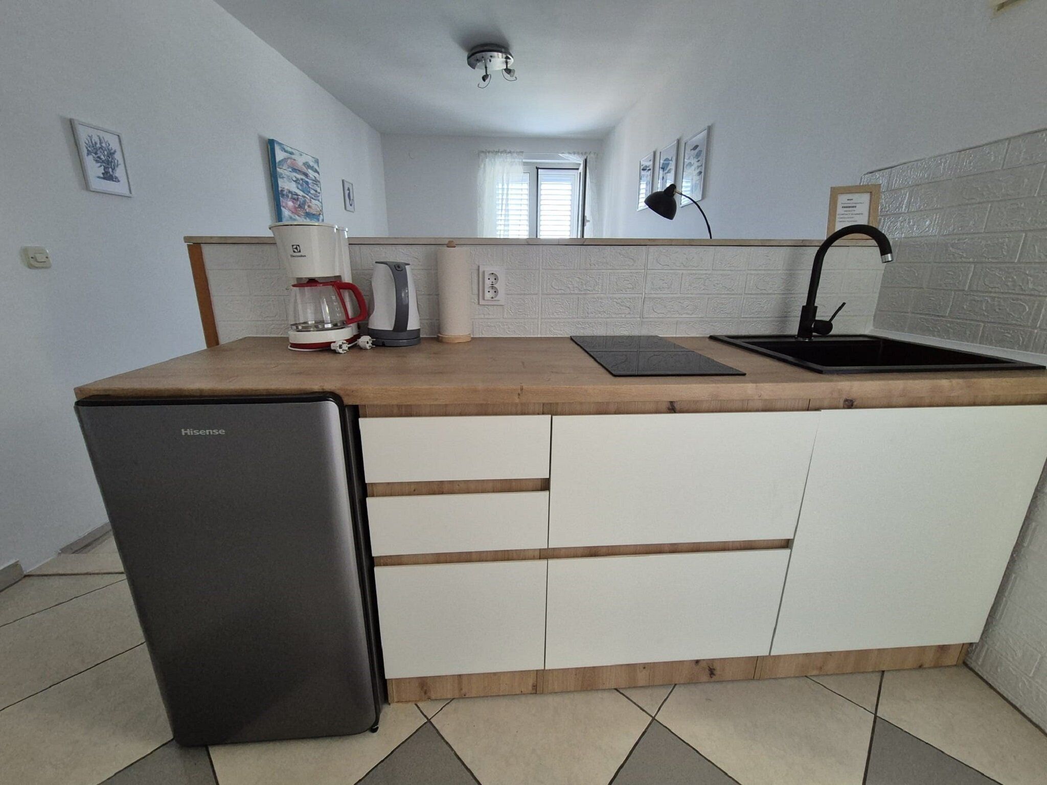 A compact kitchen with a refrigerator, a coffee maker, a kettle, and a sink.