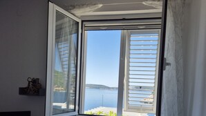 A bedroom with a large window overlooking a body of water, a bed, a TV, and a small table. - Apartments Matea (Dubrovnik)