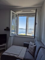 Quarto com uma grande janela com vista para um corpo de água, uma cama, uma TV e uma mesinha.