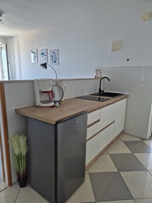 A compact kitchen with a refrigerator, a coffee maker, a sink, and a tiled backsplash. - Apartments Matea (Dubrovnik)