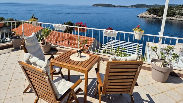 A terrace with a wooden table and chairs, potted plants, and a view of the sea. - Apartments Matea (Dubrovnik)