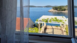 A room with a large window overlooking a coastal view, a hanging light fixture, and a view of a terrace with greenery. - Apartments Matea (Dubrovnik)