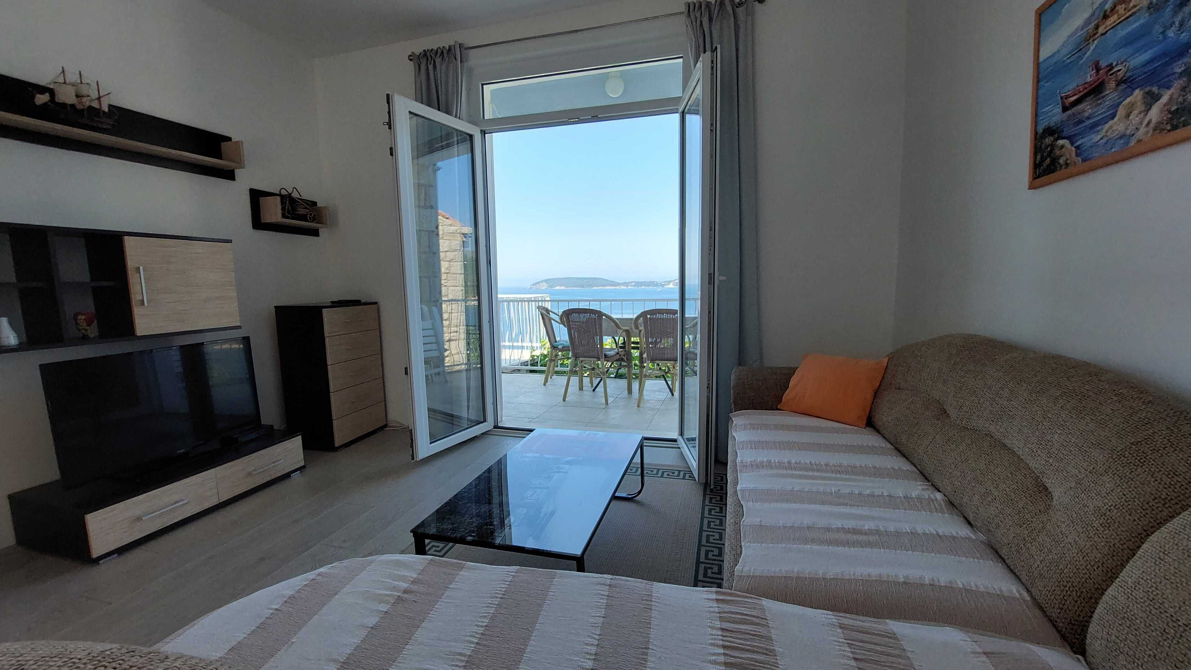 Een moderne woonkamer met een bank, televisie en een balkon met uitzicht op zee.