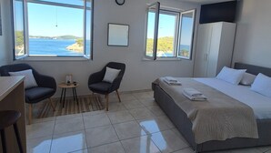 A hotel room with a bed, two chairs, a small table, a clock, and large windows with a view of the sea. - Apartments Matea (Dubrovnik)
