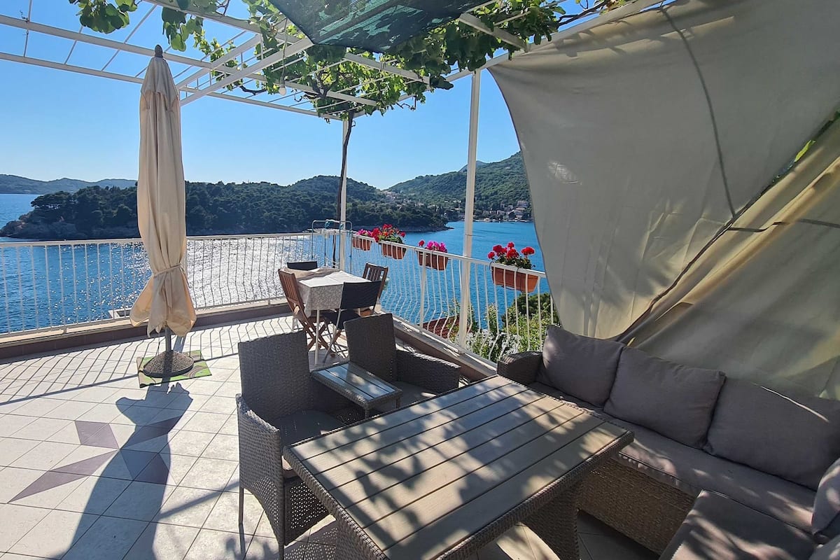 Terraço ao ar livre com mesa, cadeiras, um sofá e plantas em vasos.