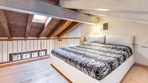 A bedroom with a bed, wooden ceiling beams, a skylight, a railing, and a wall-mounted light fixture. - Holiday Apartment "Rosalba" At the Foot of Monte Baldo with Balcony and Views (Ferrara Monte Baldo)