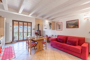 Un coin repas avec une table et des chaises en bois, un canapé rouge et une vue dégagée grâce à de grandes portes vitrées.