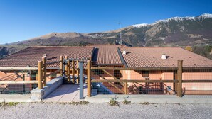 A building with a tiled roof, a fenced area, and a mountainous backdrop. - Holiday Apartment "Rosalba" At the Foot of Monte Baldo with Balcony and Views (Ferrara Monte Baldo)