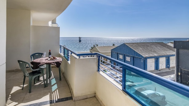 Ein Balkon mit Tisch und Stühlen, mit Blick auf ein Gewässer und Gebäude.