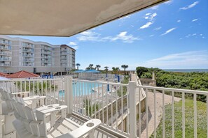 A pool area with a view of a hotel building, a wooden deck, and a clear sky. - Beautifully Updated Oceanfront Condo w/ wine fridge (North Topsail Beach)