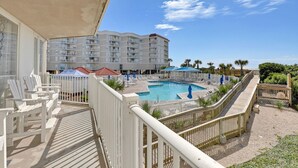 Ein Hotelbalkon mit Pool, weißen Stühlen und Blick aufs Meer.