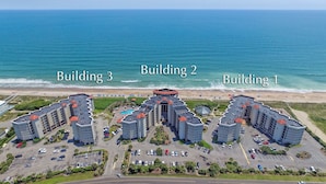 Ett hotellkomplex vid stranden med tre byggnader, var och en med en egen, tydlig arkitektonisk stil och en pool på taket.