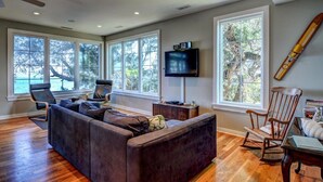 A living room with a sectional sofa, a television, and a large window overlooking a scenic view. - Soundfront Home with Old World Charm! Claw foot tub, private dock (Topsail Beach)