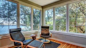A room with large windows, two leather chairs, a small round table, and a view of trees and water. - Soundfront Home with Old World Charm! Claw foot tub, private dock (Topsail Beach)