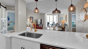 Een moderne keuken met een marmeren aanrecht, een spoelbak en een eetgedeelte met een tafel en stoelen. Er hangen hanglampen boven de keuken en de eethoek.