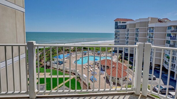 Uitzicht vanaf een balkon op een zwembad, strand en oceaan.