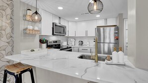 Een moderne keuken met witte kasten, een groot kookeiland, roestvrijstalen apparatuur en decoratieve verlichting.