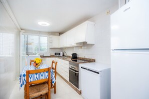 Een compacte keuken met witte kastjes, een magnetron, een oven en een vaatwasser.