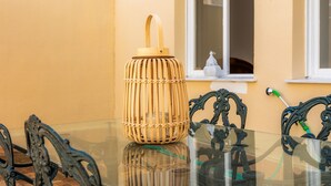 Une table en verre, une lanterne en osier, des chaises en métal décorées et une fenêtre à cadre blanc.