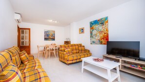 Un salon avec un canapé, un téléviseur, une table basse et un tableau accroché au mur.