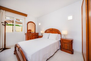 Een slaapkamer met een houten bed, nachtkastjes, een spiegel en een raam met gordijnen.