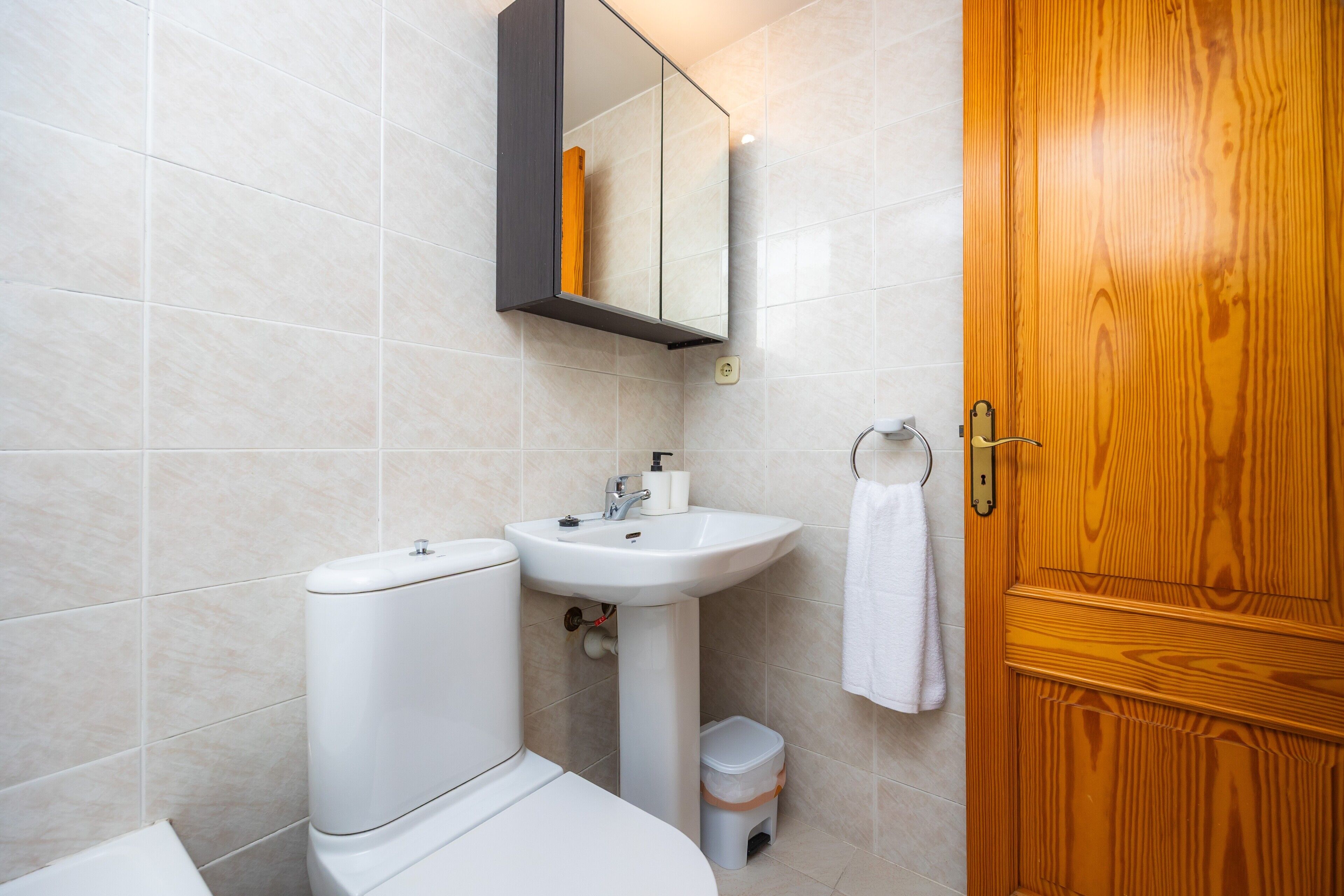 A bathroom with a toilet, sink, mirror, and wooden door.