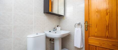 A bathroom with a toilet, sink, mirror, and wooden door.