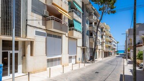 Une rangée d’immeubles à plusieurs étages dotés de balcons, un ciel dégagé et une mer visible à l’arrière-plan.