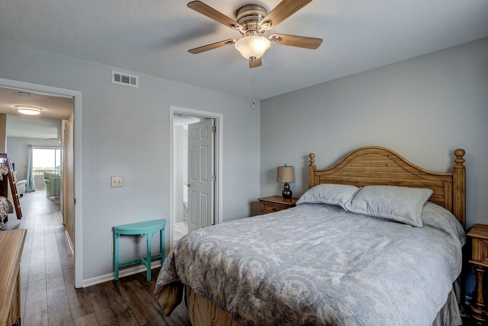 A bedroom with a wooden bed, a ceiling fan, a small table, and a door leading to another room.