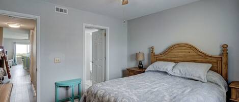 A bedroom with a wooden bed, a ceiling fan, a small table, and a door leading to another room.