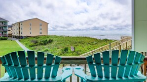 A balcony with two green Adirondack chairs facing a beach, a sign indicating a protected area, and a building in the background. - Oceanfront Condo, Steps Away from the beach access (Surf City)