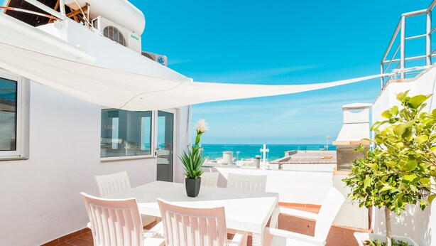 Una terraza con muebles blancos, una planta en maceta y vista al mar.
