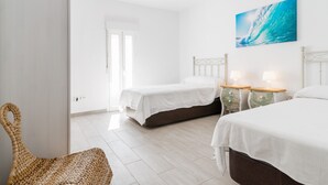 Una habitación con dos camas, una silla de mimbre y un cuadro de una ola en la pared.