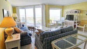 Un salon avec un canapé, une table et un meuble pour la télévision. Il y a un balcon avec des chaises et une table.
