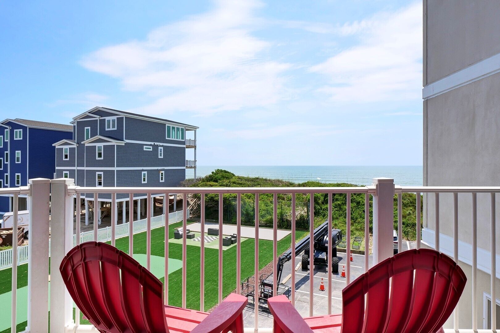 Un balcon avec des chaises rouges, une vue sur la mer et, au loin, un chantier de construction.