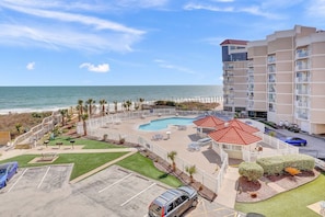 A hotel with a pool, beach view, and a parking area.