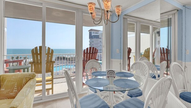Un balcone con vista sull'oceano, una piscina e un'area pranzo con sedie e tavolo.