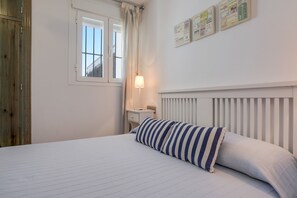 Une chambre à coucher avec un lit, une table de chevet, une lampe, une fenêtre et un mur orné de tableaux.