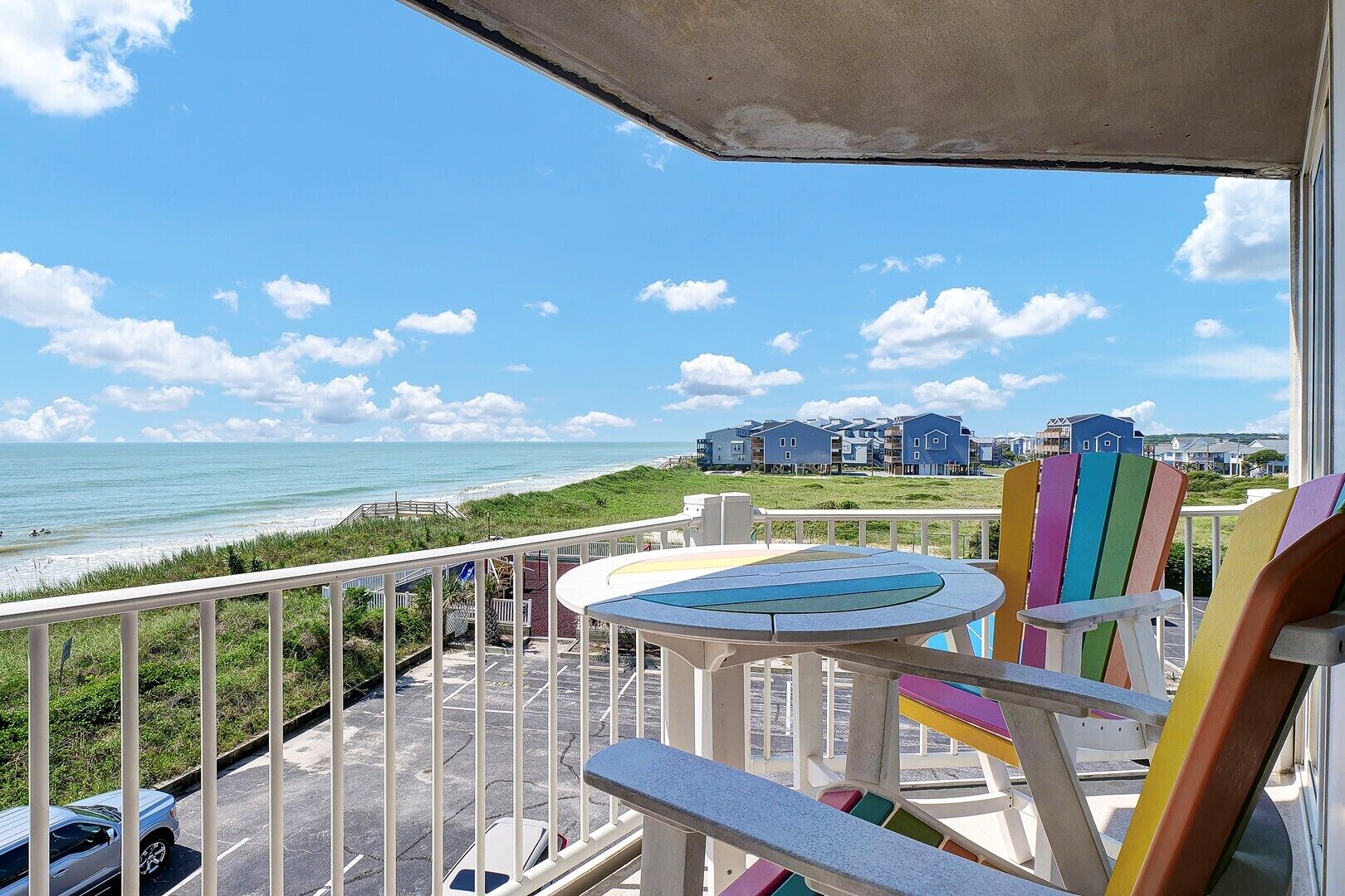 Ein Balkon mit Tisch und bunten Stühlen mit Blick auf Strand und Meer.