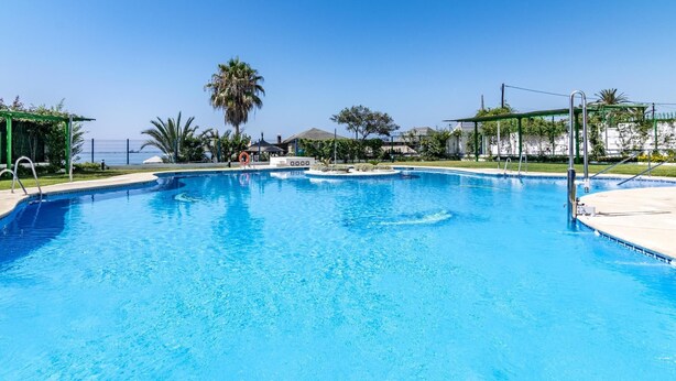 A clear blue swimming pool with a palm tree in the background, surrounded by a fence and greenery. - Apartamento en Marbella con vistas laterales al mar 328 (Marbella)