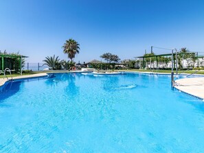 A clear blue swimming pool with a palm tree in the background, surrounded by a fence and greenery. - Apartamento en Marbella con vistas laterales al mar 328 (Marbella)