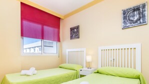 A hotel room with two single beds, each with a green bedspread and white towels. There is a window with a red blind, a white bedside table with a lamp, and two wall-mounted paintings. - Apartamento en Marbella con vistas laterales al mar 328 (Marbella)