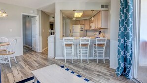 A compact kitchen with white bar stools, a dining table, and a refrigerator. - Adorable Updated Oceanfront Condo on the top floor! (North Topsail Beach)