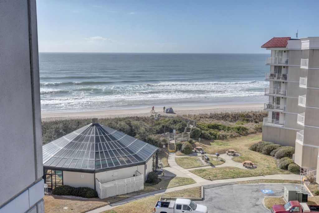 A coastal hotel with a beach view, a glass-roofed structure, and a parking area.
