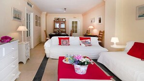 Quarto de hotel com cama, escrivaninha e cadeira. Há uma janela, uma porta e uma parede com quadros.