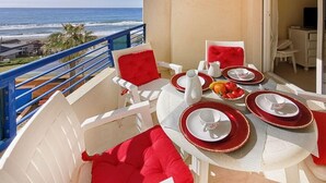Varanda com mesa posta para dois, cadeiras brancas com almofadas vermelhas e vista para o mar.