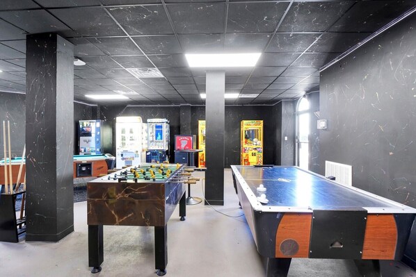 A room with two foosball tables, a pool table, and arcade games.