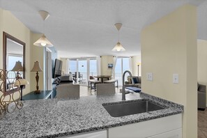 A hotel room with a kitchen area, a dining table, and a balcony with a view.
