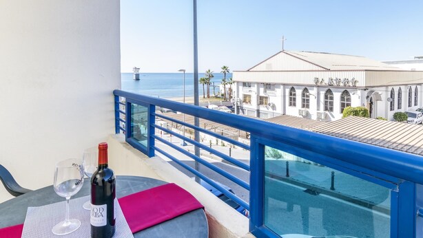 A balcony with a table set for two, a bottle of wine, and a view of a building with a cross on top. - Banana Beach (Marbella)