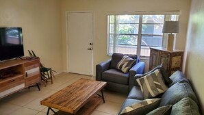 Een woonkamer met een televisie, een bank, een salontafel en een deur.